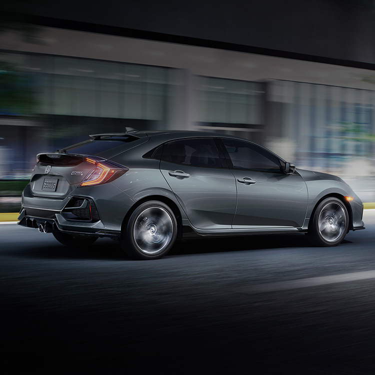 Rear passenger-side view of the 2021 Honda Civic Sport Touring Hatchback, in Sonic Gray Pearl, driving in city at night.